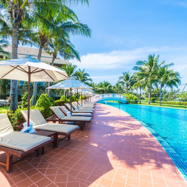 Beautiful luxury umbrella and chair around outdoor swimming pool in hotel and resort with coconut palm tree on blue sky - Boost up color Processing